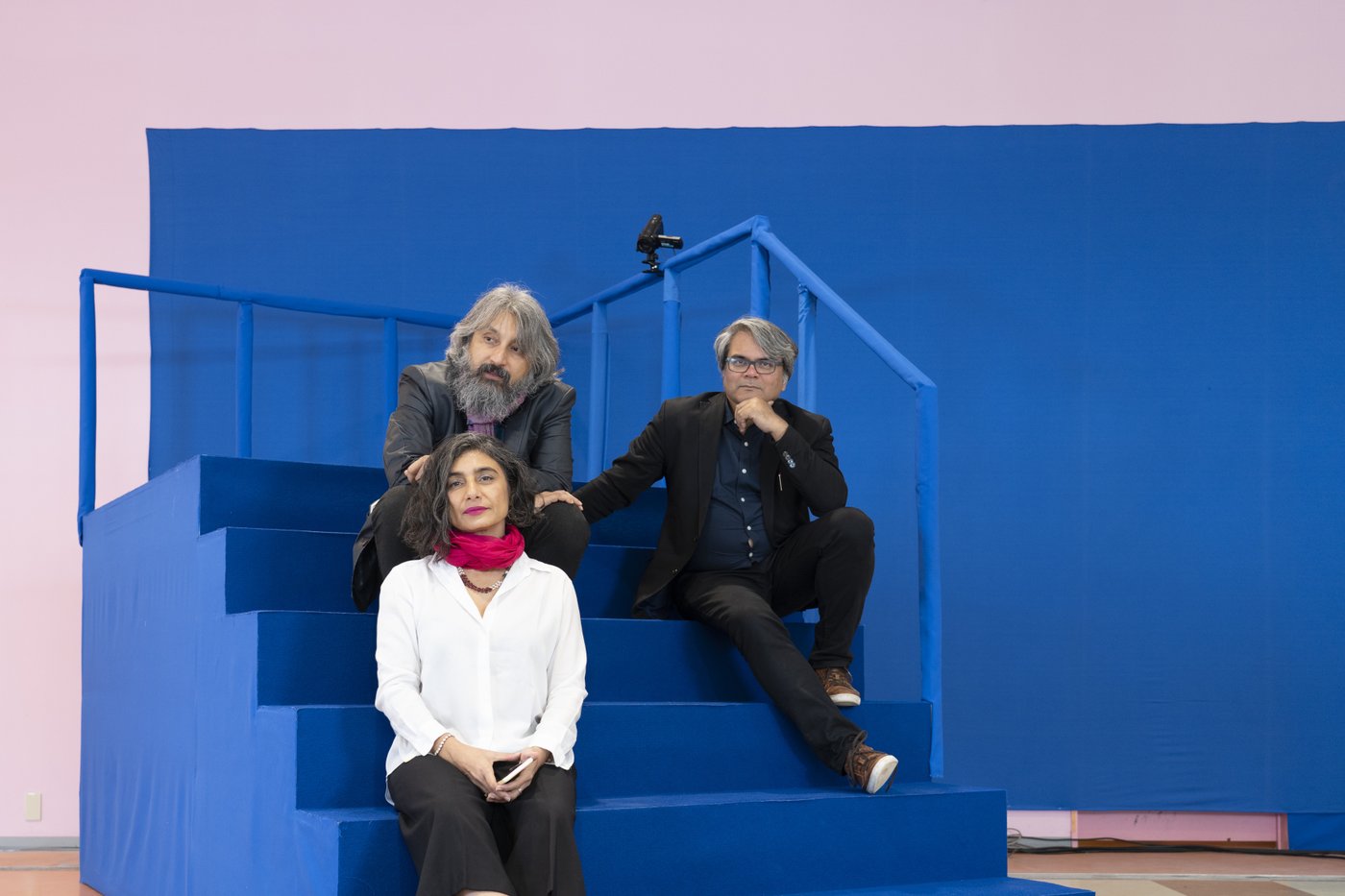 Zwei Männer und eine Frau sitzen auf einer blau gestrichenen Treppe