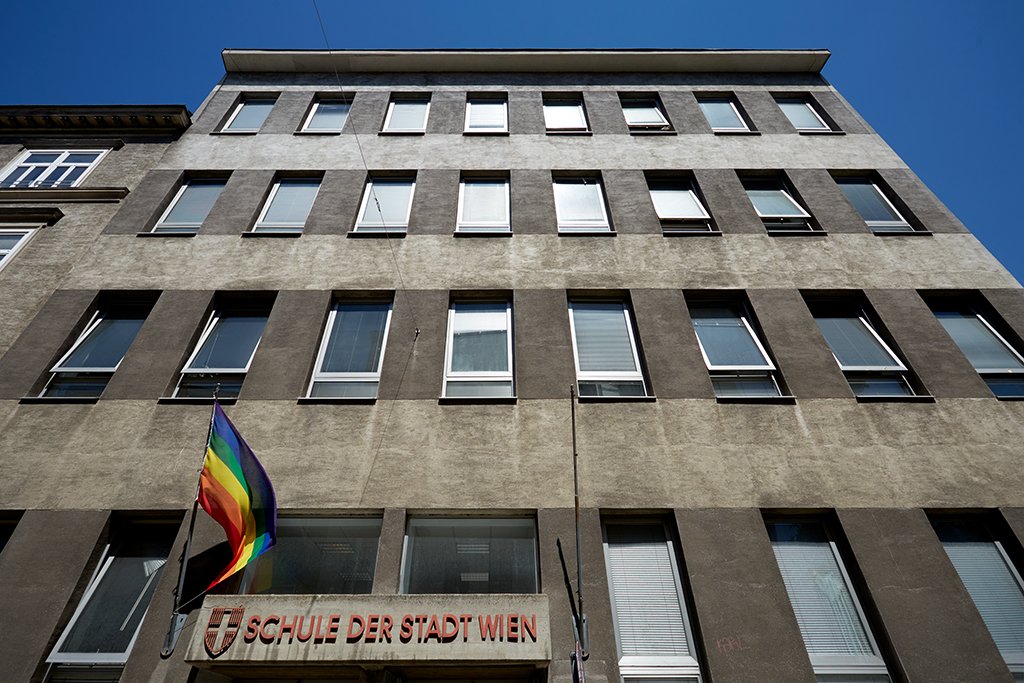 Gebäude des mit Aufschrift "Schule der Stadt Wien und Regenbogenfahne