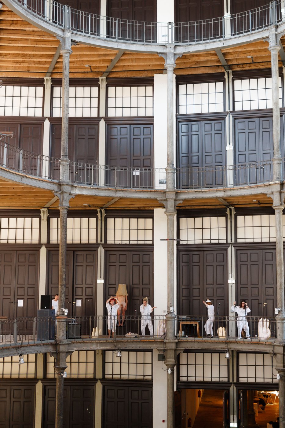 Frontale Ansicht der Galerien des Prospekthofes. Auf der untersten performen 5 Künstlerinnen in  weißen Overalls singend und tanzend.