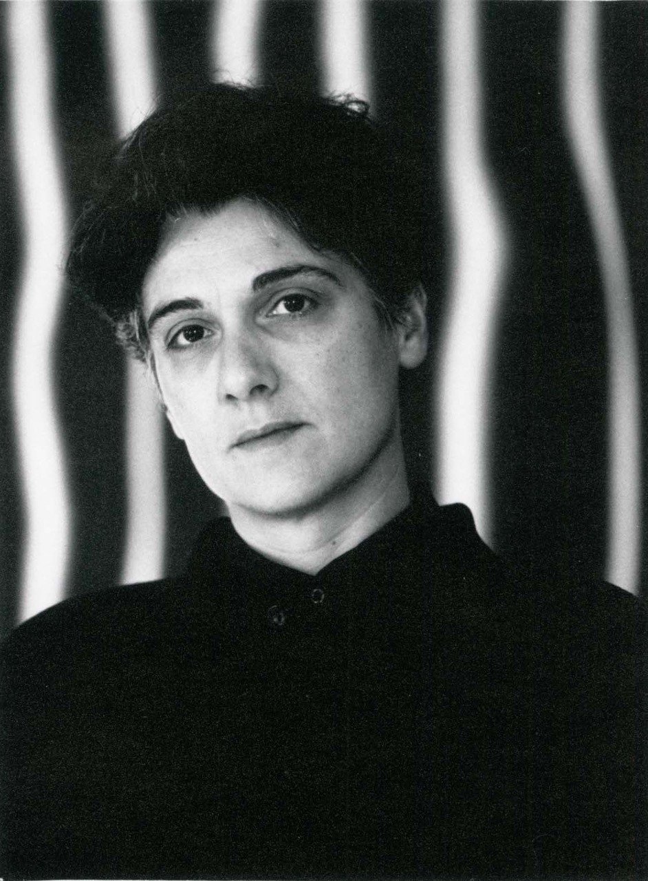 Schwarz-Weiß-Foto von Prof. Nasrine Seraji, Porträtansicht von vorne mit kurzen dunklen Haaren, schwarzer Kleidung, vor gestreiftem Hintergrund.