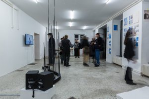 weißer Raum mit küntlerischen Installationen im Raum und an den Wänden, mehrere Personen die die Kunstwerke betrachten