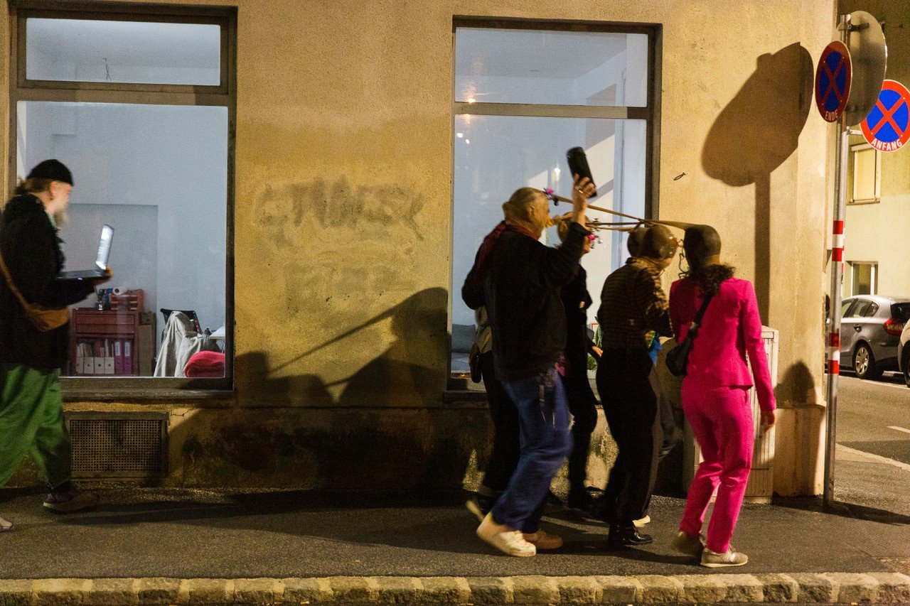 mehrere Personen mit Nylonstrumpfhosen über ihren Köpfen gehen als Gruppe eine Straße entlang