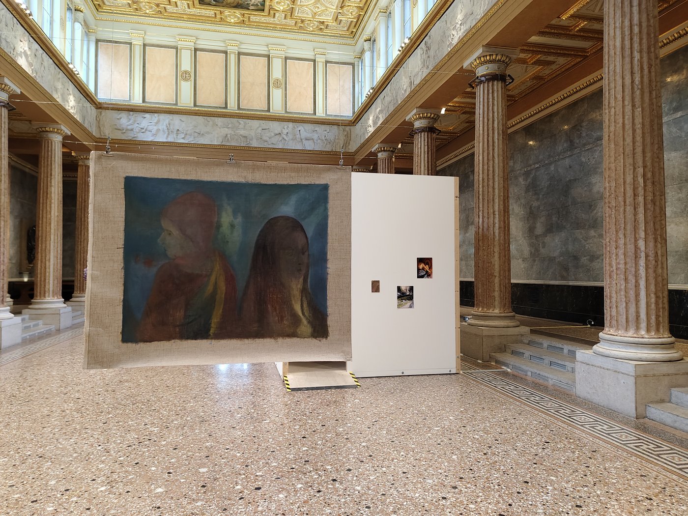 Im Vordergrund ein Werk das von der Decke hängt im Hintergrund ein white cube mit Bildern darauf