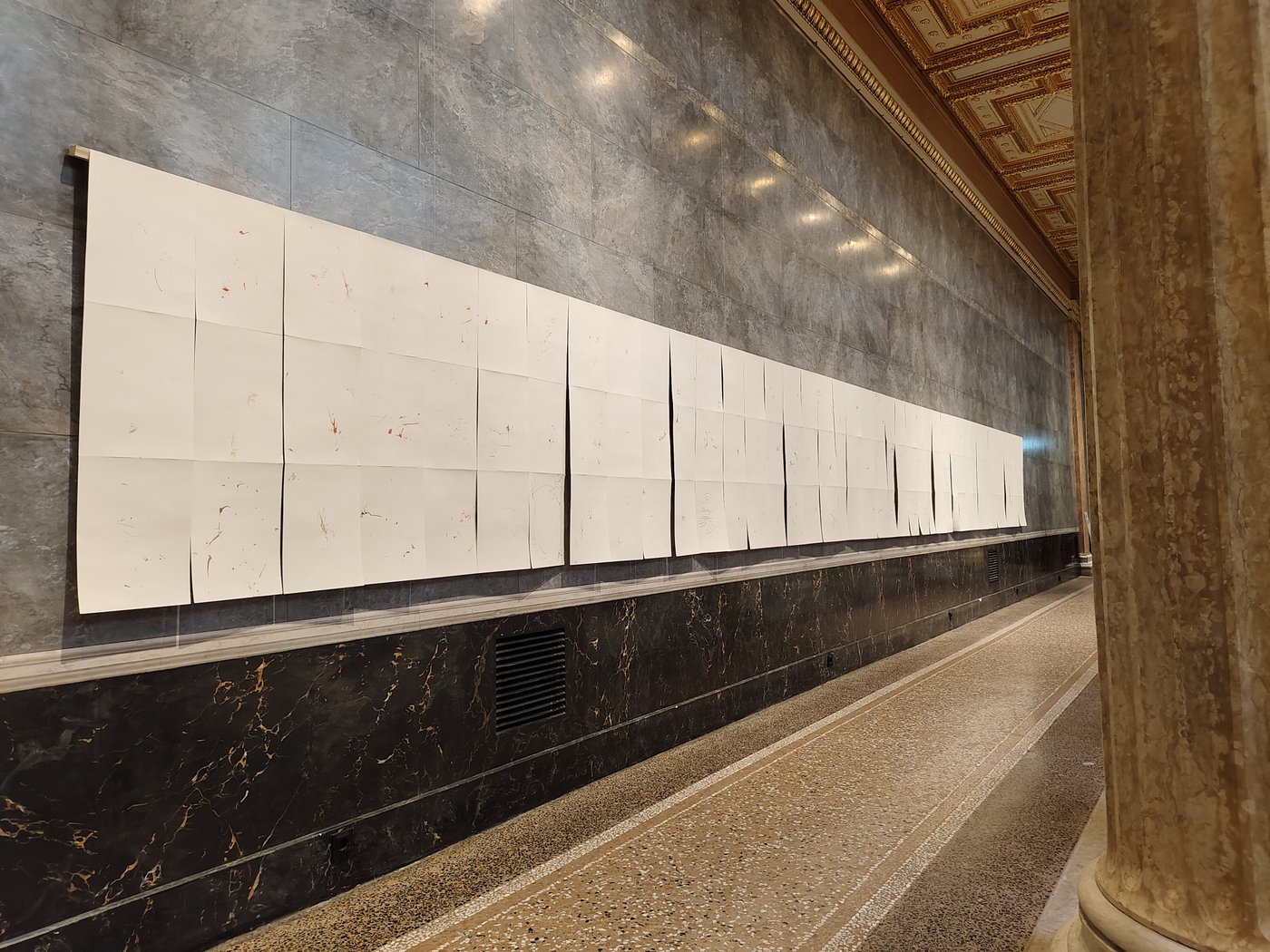 mehrere Reihen weißes Papier hängen an einer Marmorwand