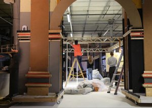 Im Vordergrund sieht man den Ausschnitt eines Tores aus Holz. im Hintergrund arbeiten drei Studierende am Aufbau einer Holzkonstruktion.