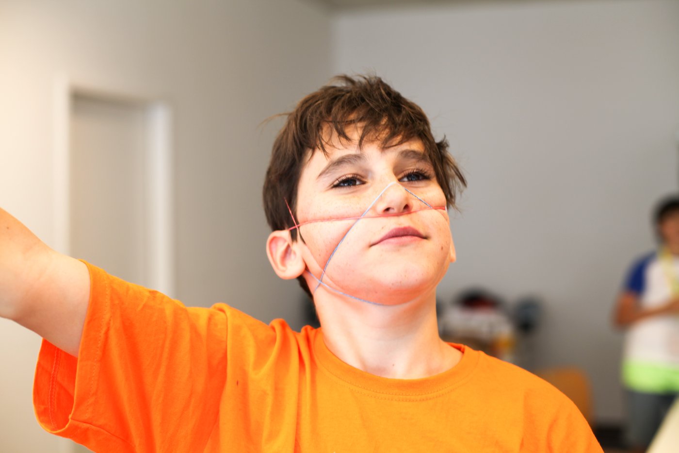 Junge mit orangem T-Shirt und einem Gummi über dem Gesicht