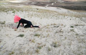 Person mit rosa Halsteil krabbelt in einer Wüstenlandschaft am Boden
