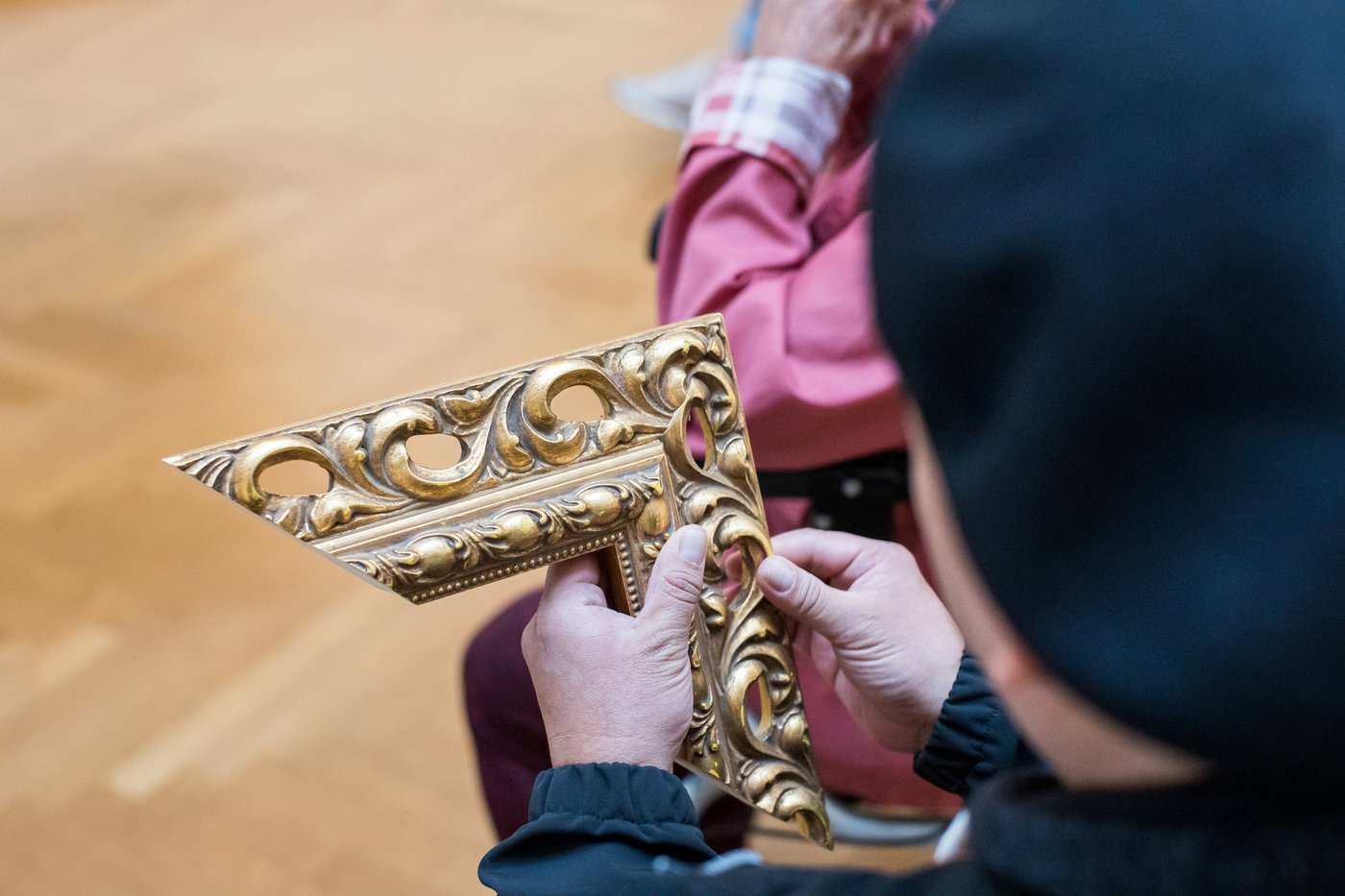 Detailfoto von Händen, die einen historischen Goldrahmen begreifen