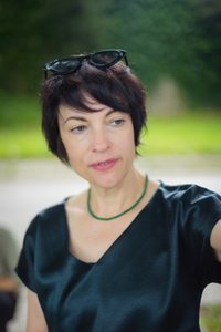 Frau mit kurzen braunen Haaren vor grünem Hintergrund  und dunklem Oberteil