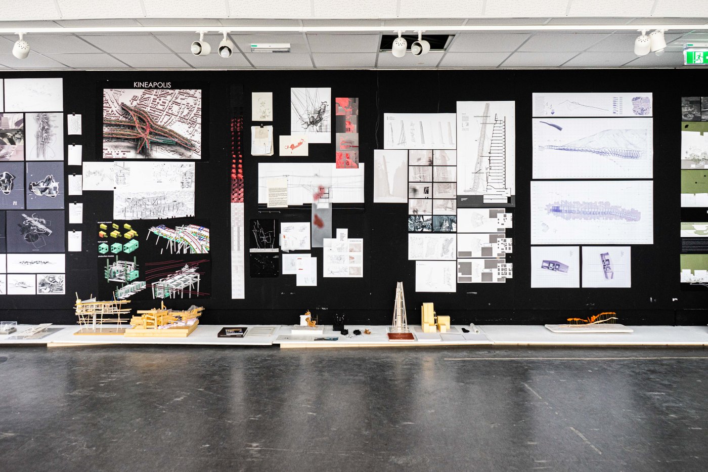 Different plans are displayed on a black wall, with corresponding architectural models in front of them on horizontal panels.