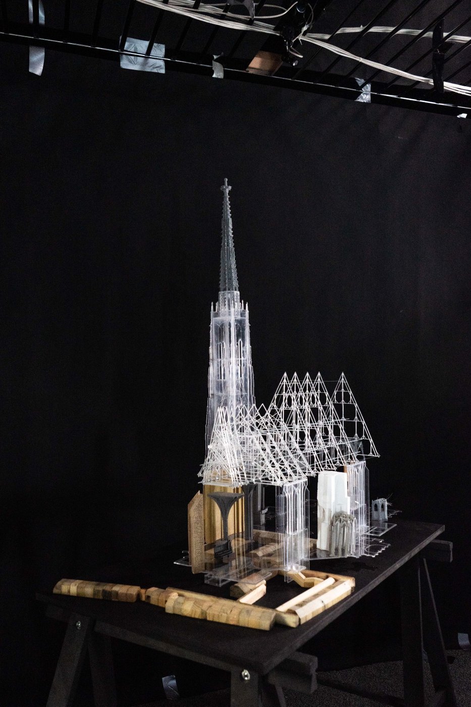 A model of St. Stephen's Cathedral in Vienna stands in front of a black background on a black table. The model consists of transparent and opaque plastic elements as well as wooden surrounding structures.