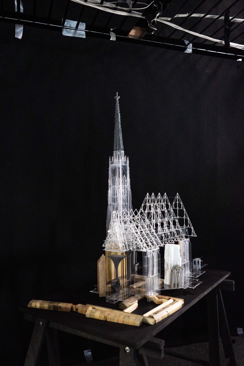 A model of St. Stephen's Cathedral in Vienna stands in front of a black background on a black table. The model consists of transparent and opaque plastic elements as well as wooden surrounding structures.
