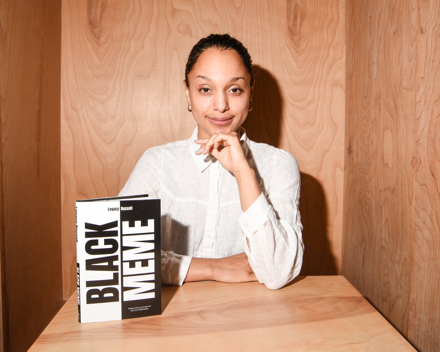 Color portrait of Legacy Russell sitting with the presented book shown on the table