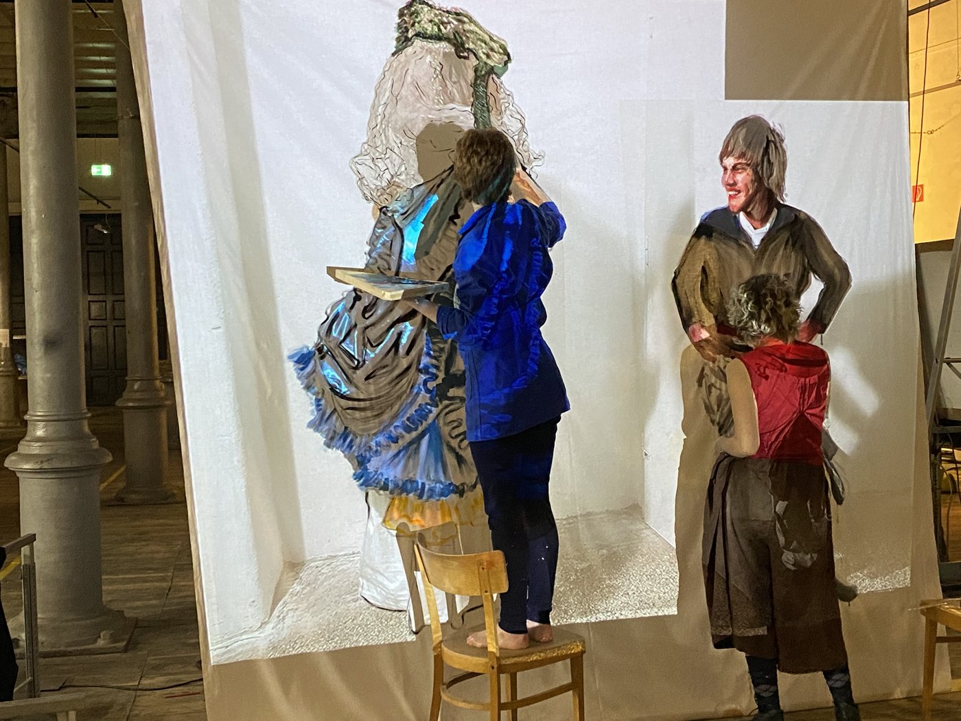 Two students stand in front of a screen onto which costumes are projected and which they paint. One of them stands on a chair.