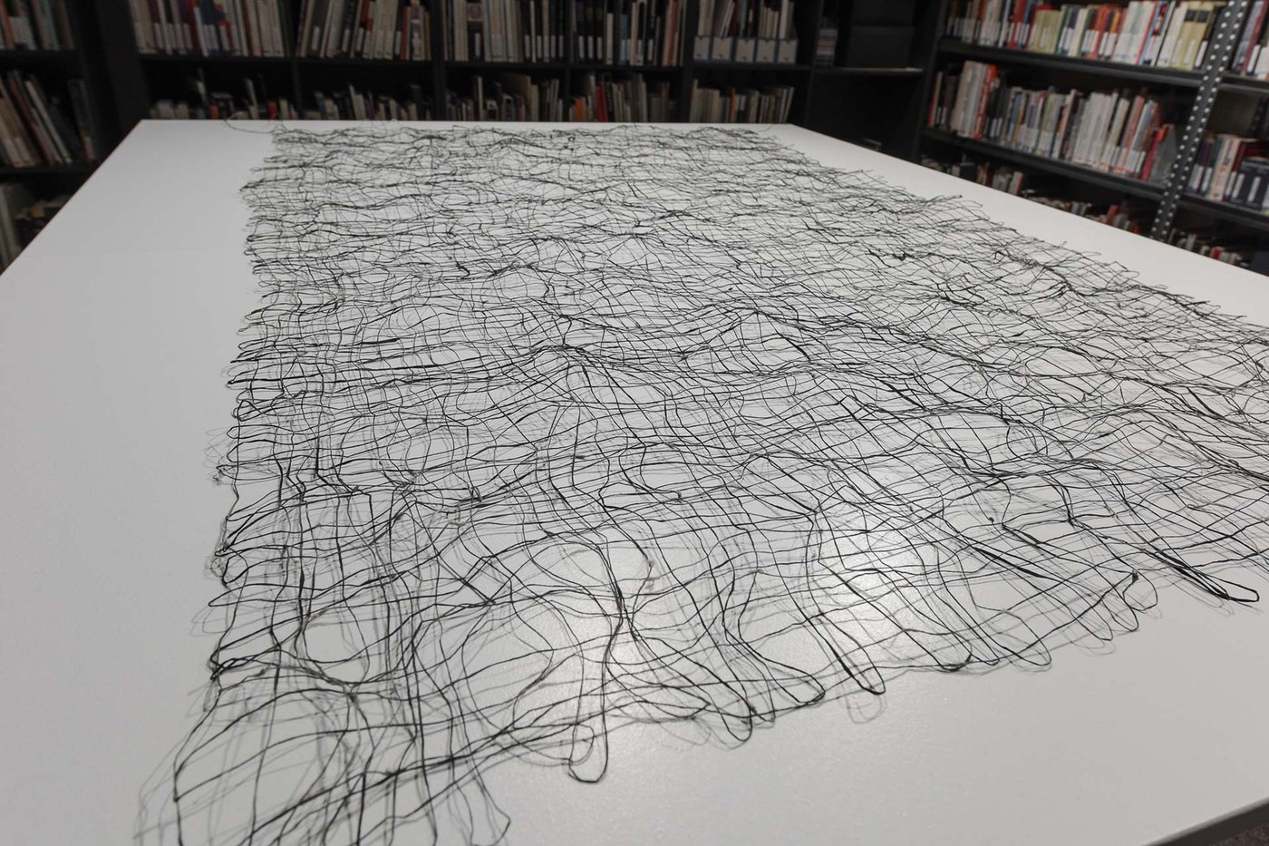 White table on which a net out of black and grayish paper threads is lying.