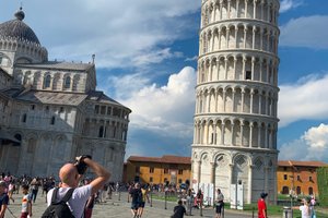 A white man, among other tourists, takes pictures of the tower of Pisa.