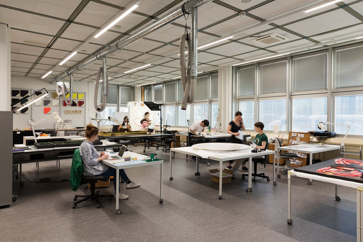 View of a large, bright studio room. On the right side a window front. There are some tables in the room on which students work.