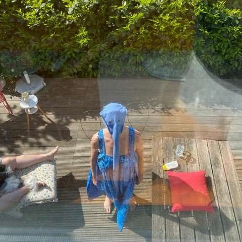 A person in a blue elephant costume is photographed from a bird's eye view. She is standing on a wooden terrace and looking up at the camera.