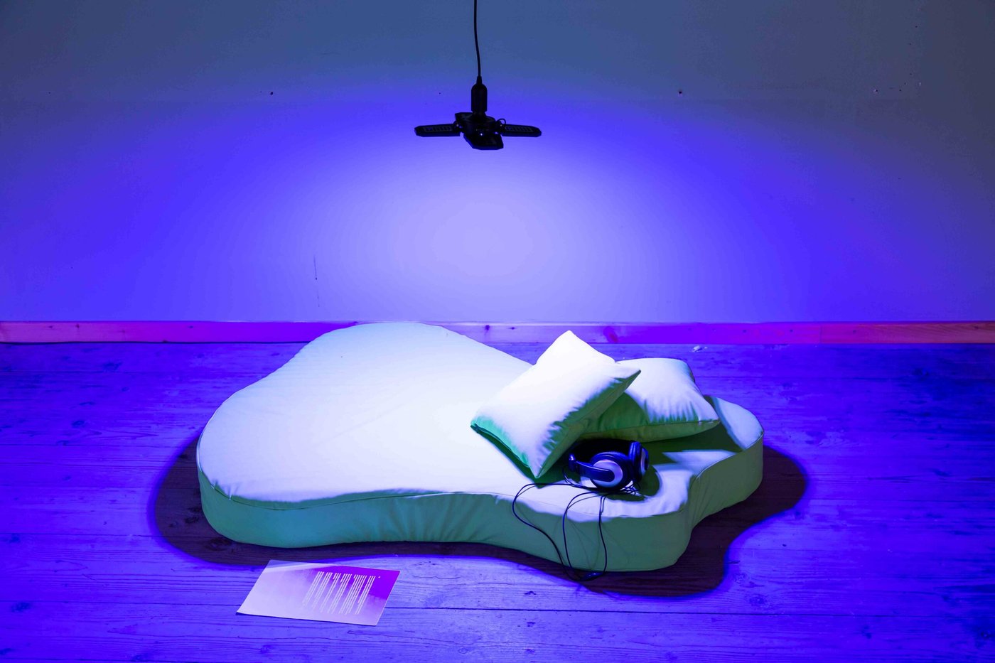 Matress an pillows on the floor with headphones on the side, in a blue lieght