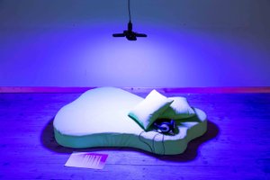 Matress an pillows on the floor with headphones on the side, in a blue lieght