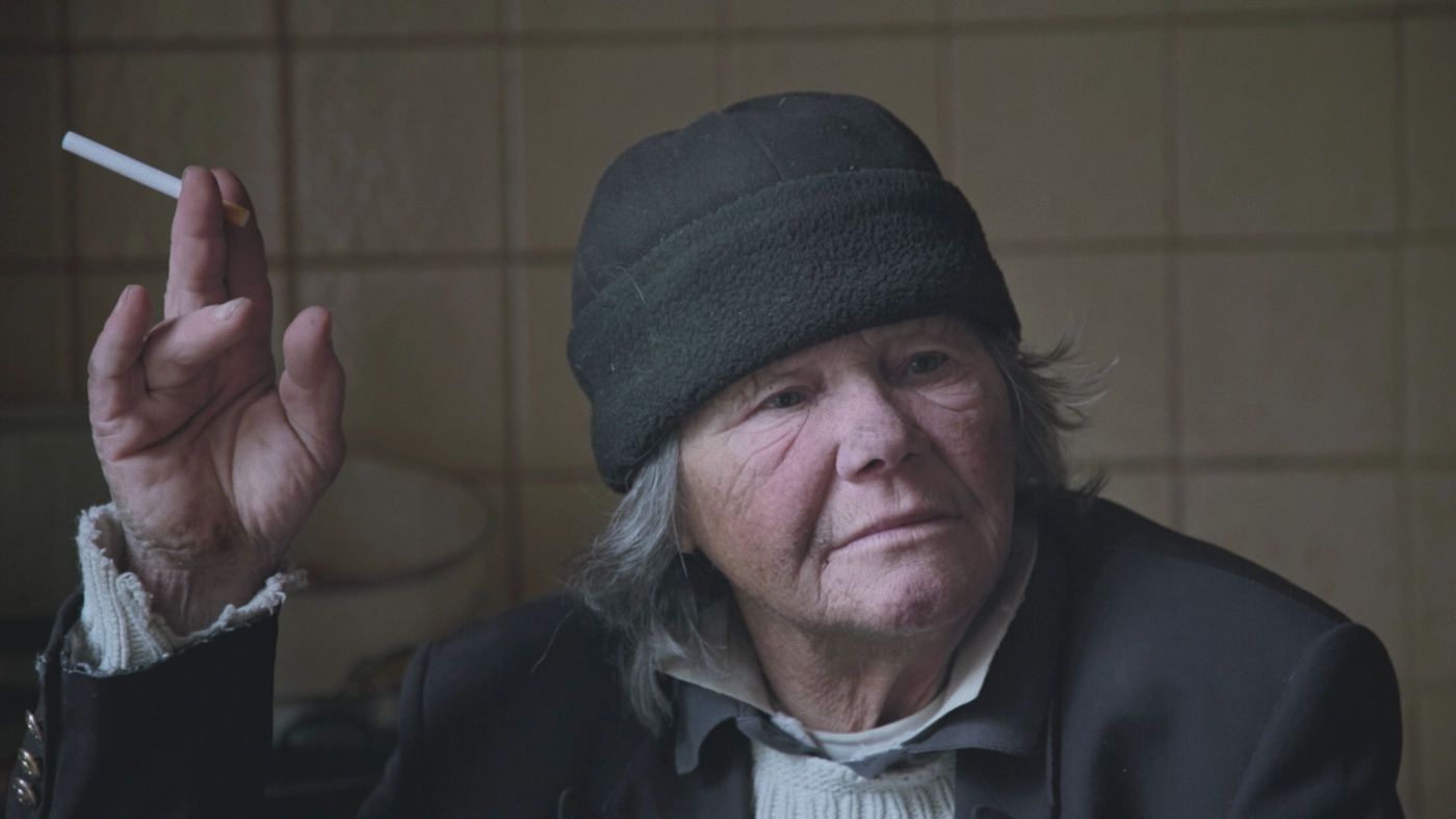 When life begins by Gabriel Monthaler and Samira Fux. AUT 2021, color, 28 min photo of an elderly person in a dark blue suit with a hood and a cigarette in his right hand