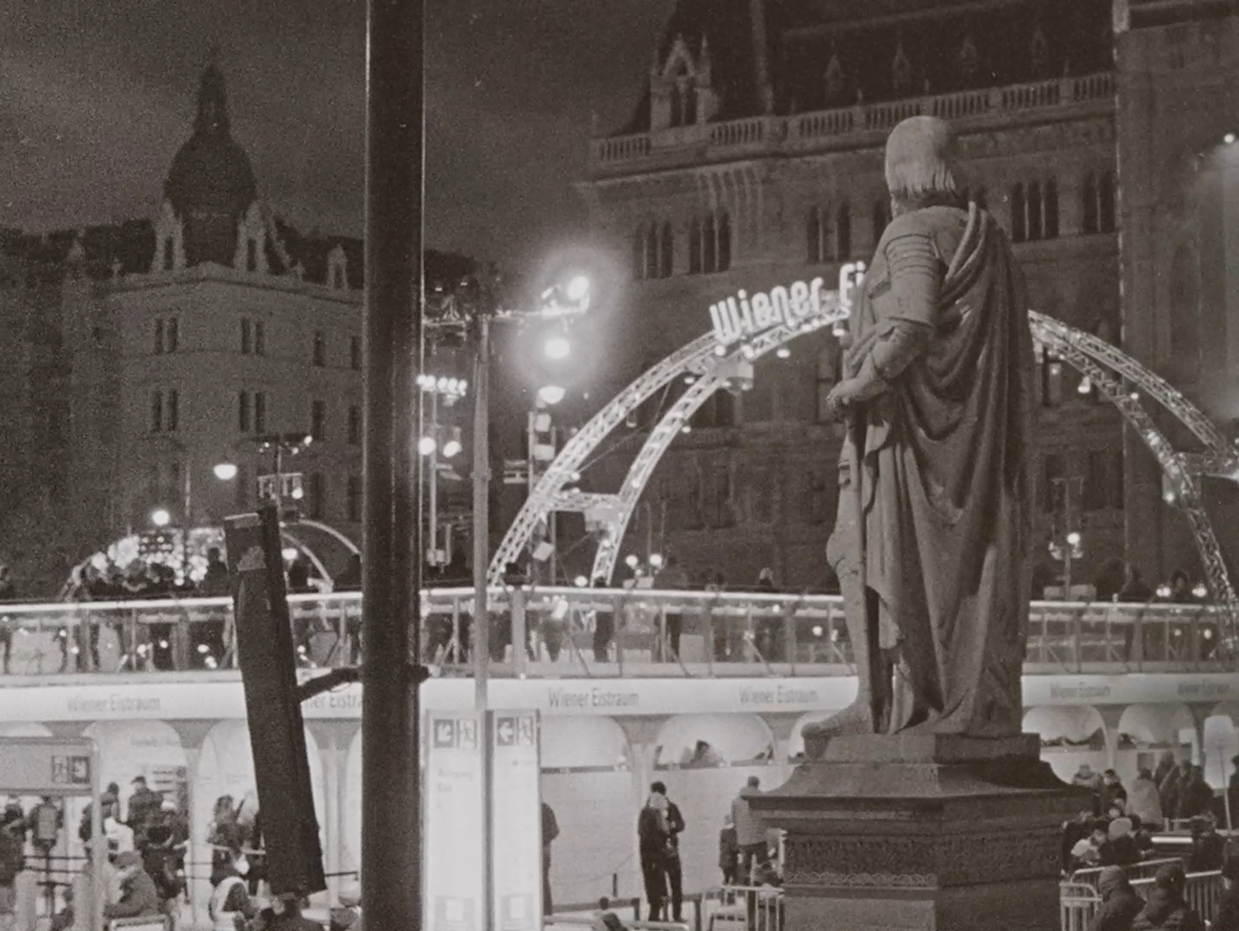 Ice Skating (16mm-practice) by Lennart Hüper and Tobias Langer. AUT 2022, B/W, 5 min black and white photo of the ice rink in front of the Vienna City Hall, in the foreground the back of a sculpture, behind it the ice rink and the City Hall