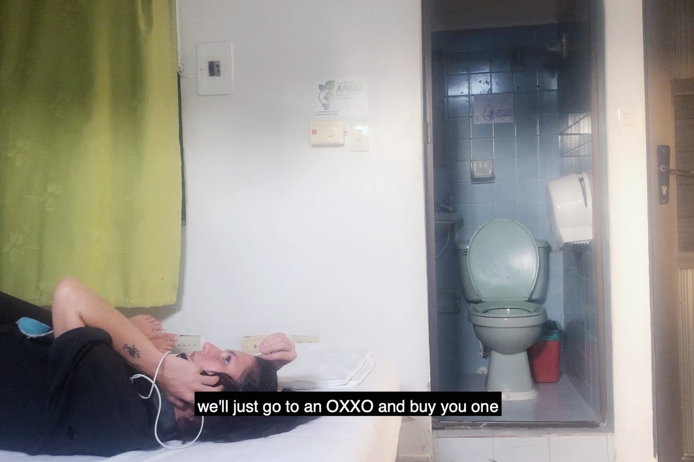 The image shows a still from the video CEREAL, a person is lying on the bed and talking on the phone, the following subtitles can be read on it "we'll just go to an OXXO and buy you one".