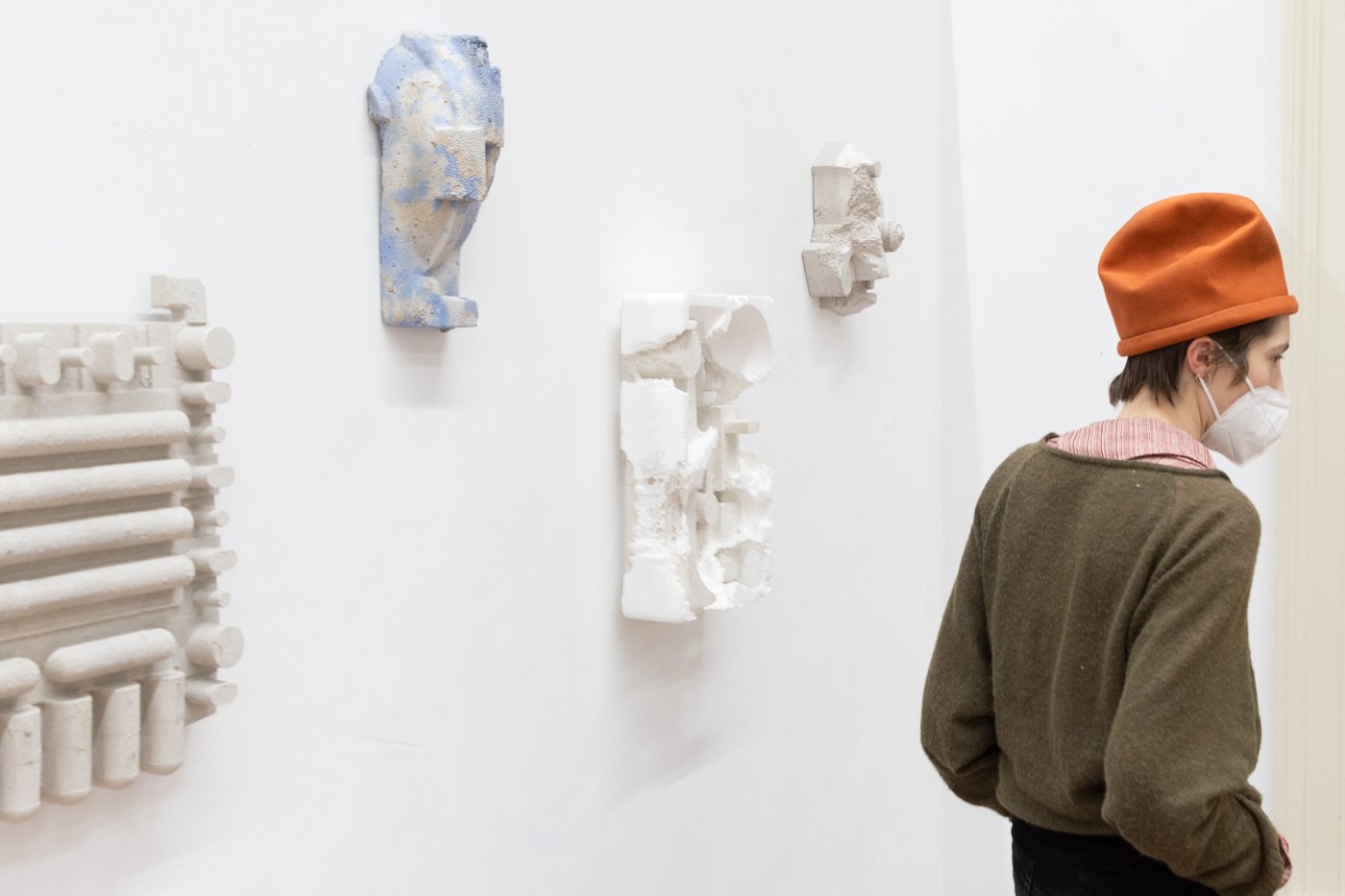 Visitor with striking orange hat in front of a wall with white abstract wall sculptures