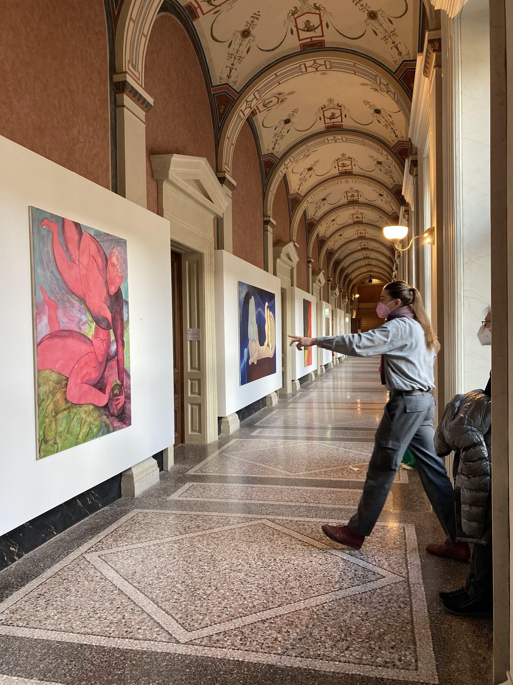 First floor, Schillerplatz 3.  In the corridor, the students' paintings of the class for figurative paintings are on display. Clemens Grömmer points with his hand to a painting by Alberto Cappai. Also visible is a work by Arang Choi.