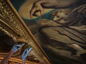 Close-up of the ceiling painting of the Aula, a hand with a sponge cleans the gold frame around the painting