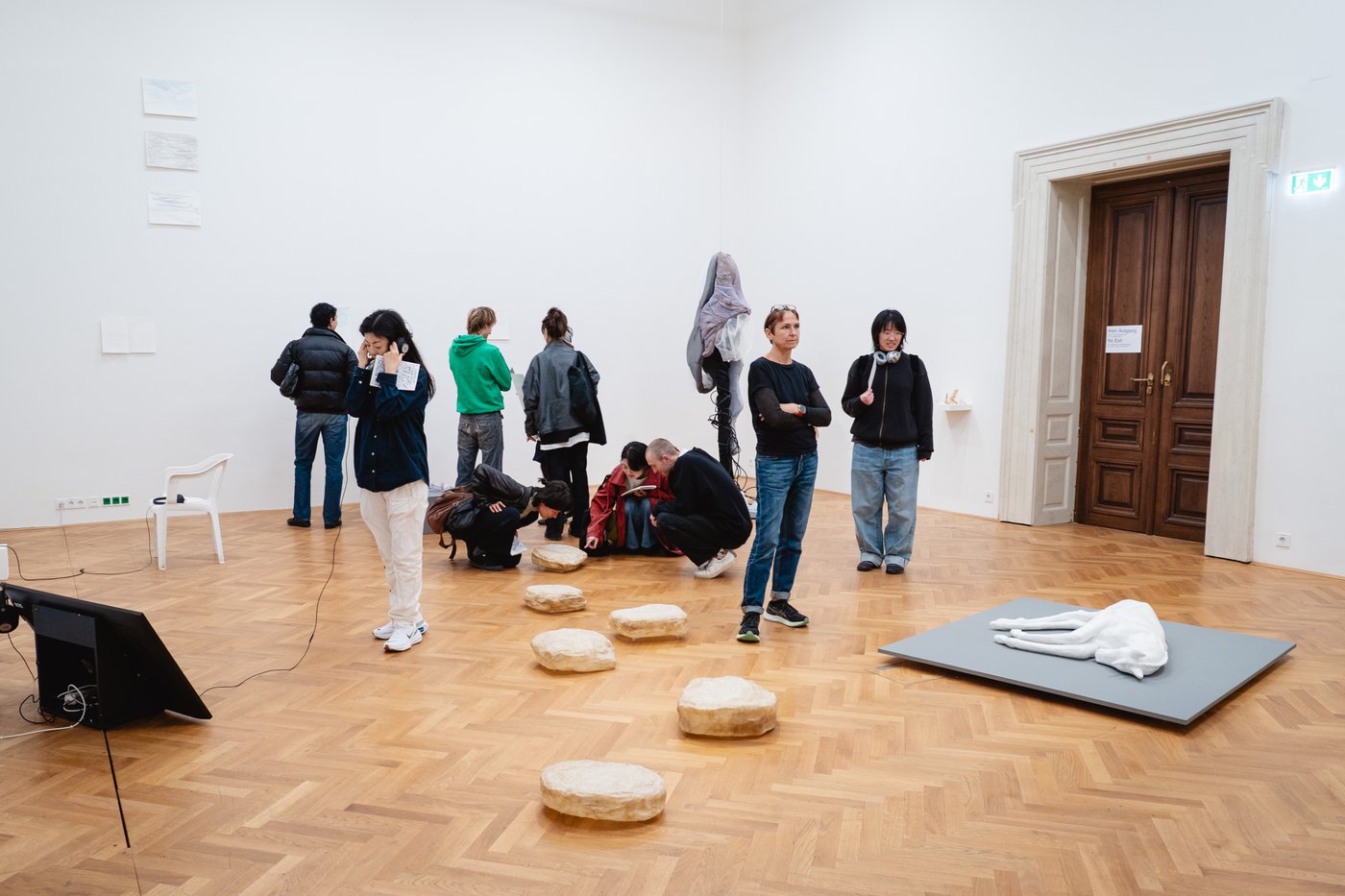 Many people in the exhibition room looking at artworks, listening to the work with headphones and speaking to each other