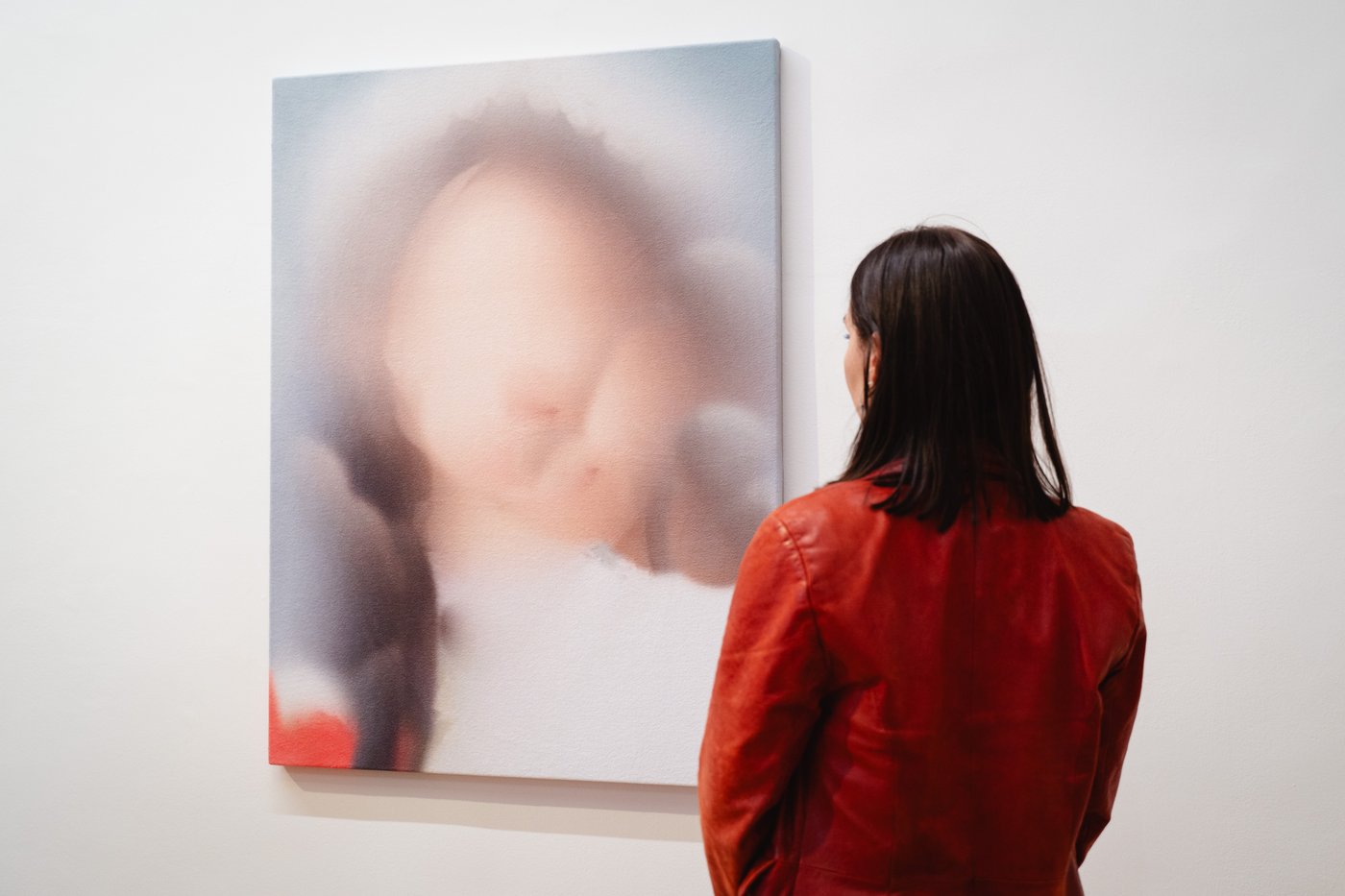 Person with red jacket looking at a painting with a unclear face