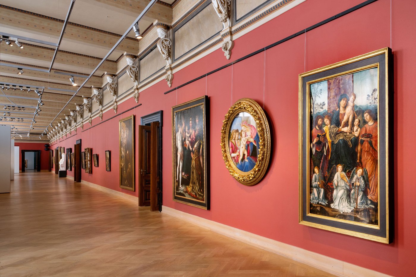 a few people watch a few paintings in a long red exhibition room