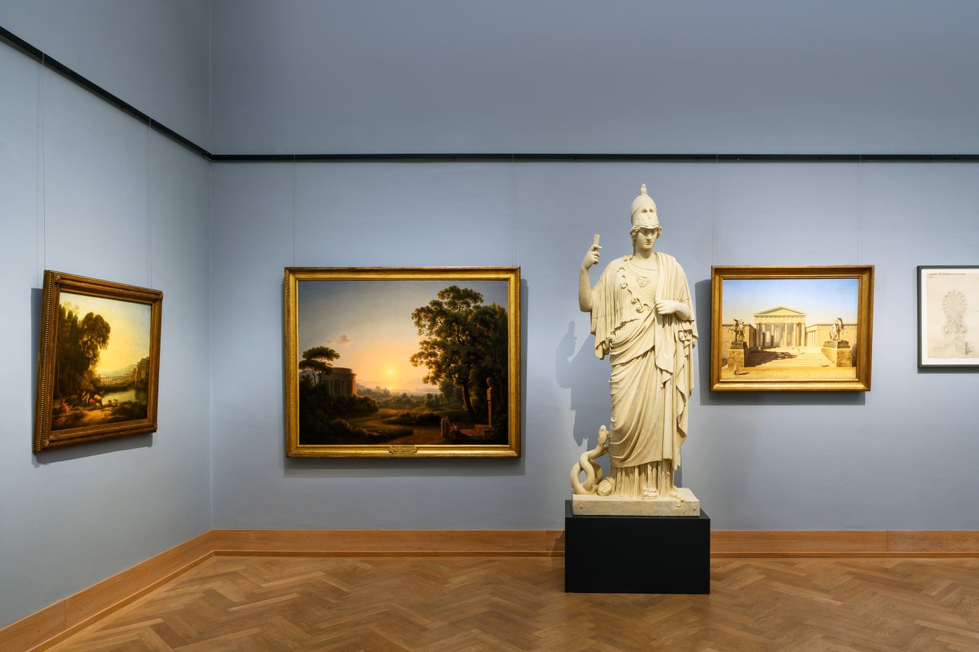 exhibition view with paintings on the wall and a greek statute