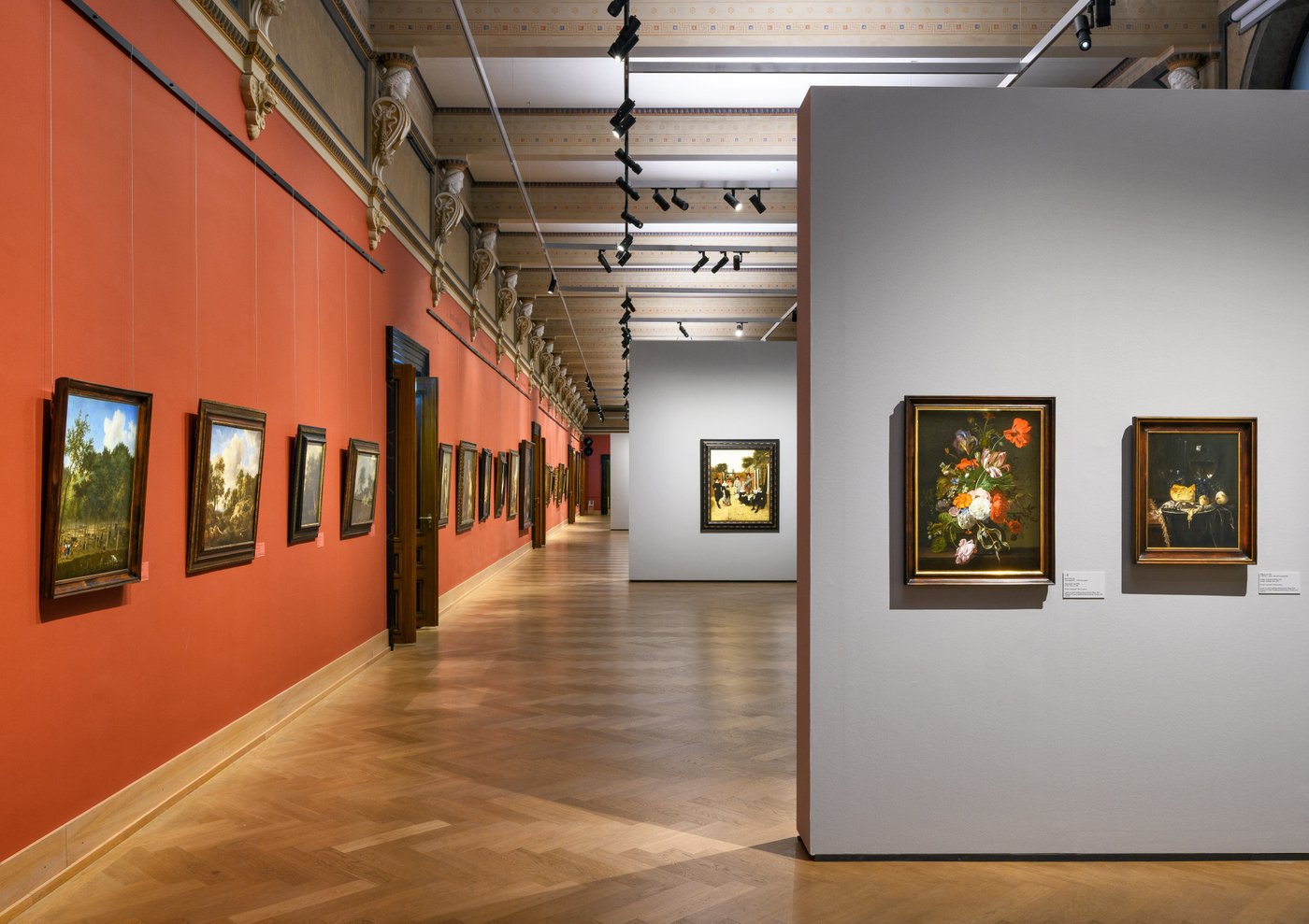 long red painted wall in a long exhibition room with historic oil paintings on the wall