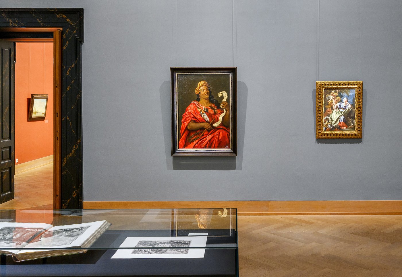 exhibition room with a glas vitrine and oil paintings on the wall