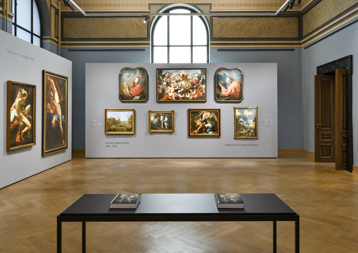a blue grey painted exhibition room in an old building with framed old paintings on the wall