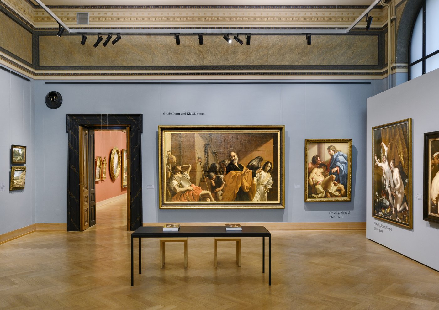 a blue grey painted exhibition room in an old building with framed old paintings on the wall