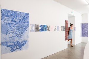 Person walking through the exhibition, on the wall are many paintings in blue and purple
