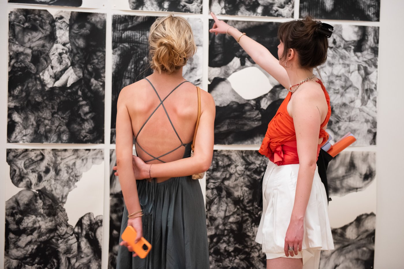zwei Frauen stehen vor den Druckgrafiken an der Wand und deuten auf eines