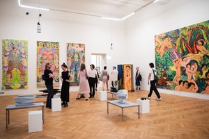 Ausstellungsansicht mit vielen Personen und bunten großen Gemälden von Figuren an der Wand