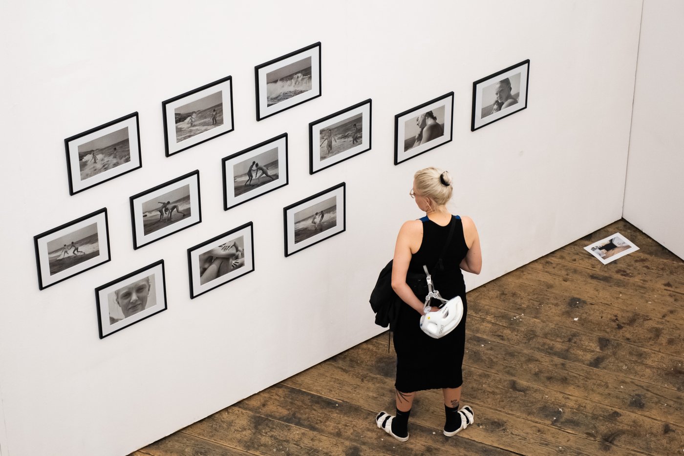 A women in a black dress looking at black and white photos on a wall