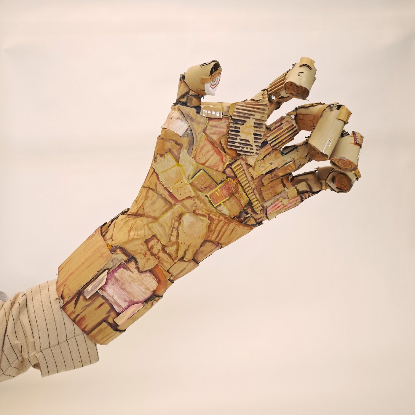 Artistic work of a hand made from cardboard scraps and small paper clips, predominantly in shades of brown.