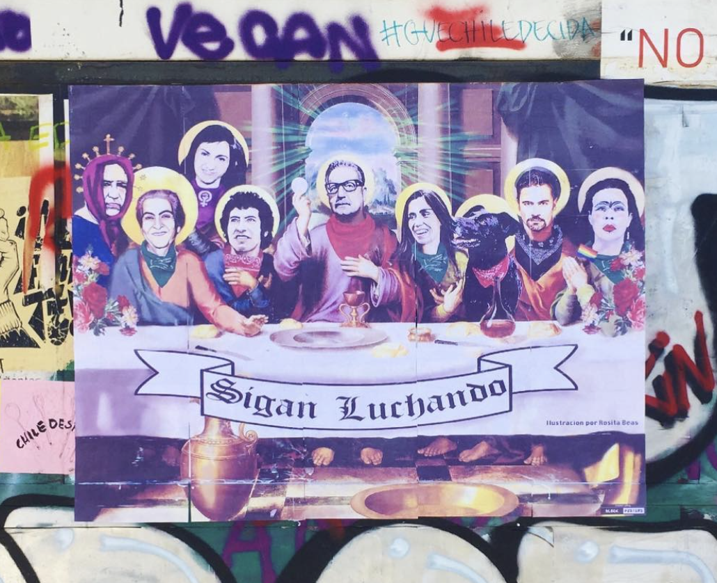 A colourful street poster depicting the Last Supper. Several figures with golden halos are seated around a table; the central figure, wearing red robes, holds a white host aloft. The figures wear green and purple scarfs. A black dog also sits at the table. In the foreground, a white banner reads "Sigan Luchando" ("Keep Fighting").