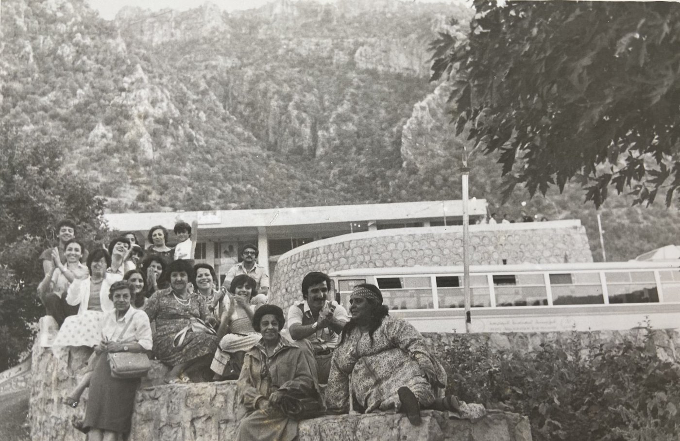 Black and white photo, group photo, people on stone wall/steps, mountains in the background