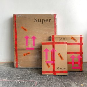 Three boxes of different sizes with red tape and the inscription Super (Art) Market lean against a white wall.