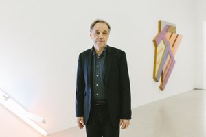 Picture of a man in a black suit in front of an artwork on the wall