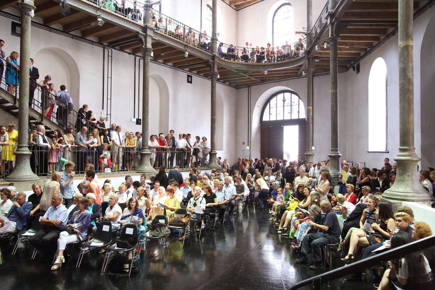 Many people are waiting in the Prospekthof (large high space over 4 floors with galleries on each floor) for the start of the 2016 graduation ceremony of the Academy of Fine Arts Vienna.
