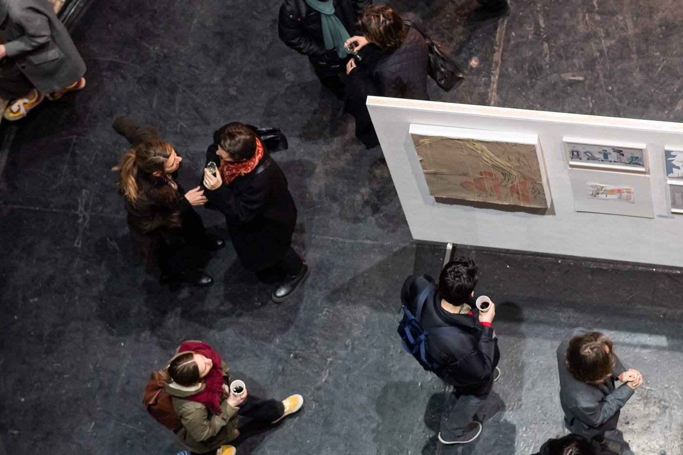 picture of people from above, they are talking and looking at artworks on a white wall