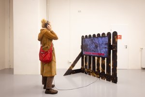 Person with headphones in front of a screen on a fence